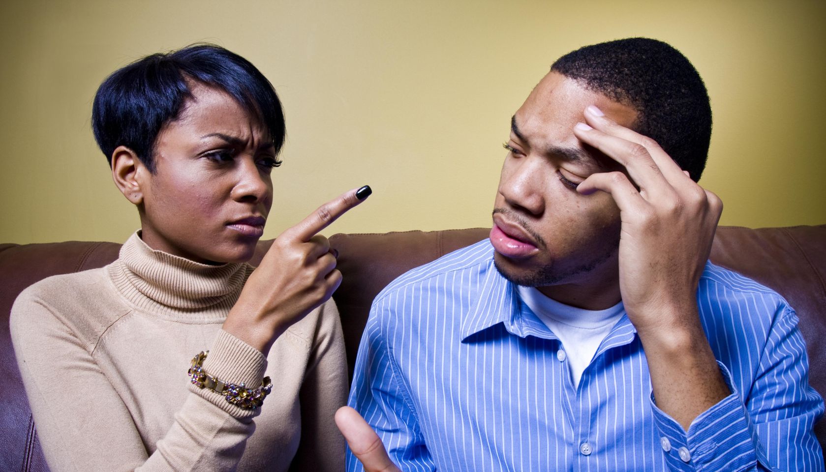 A couple is fighting on a couch and the girl is pointing her finger accusingly at him.