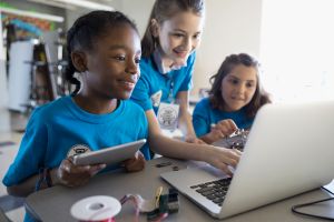 Pre-adolescent girls programming electronics at laptop and digital tablet in classroom
