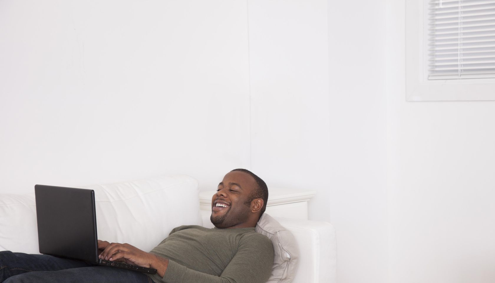 Black man laying on sofa using digital tablet