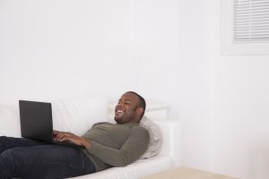 Black man laying on sofa using digital tablet