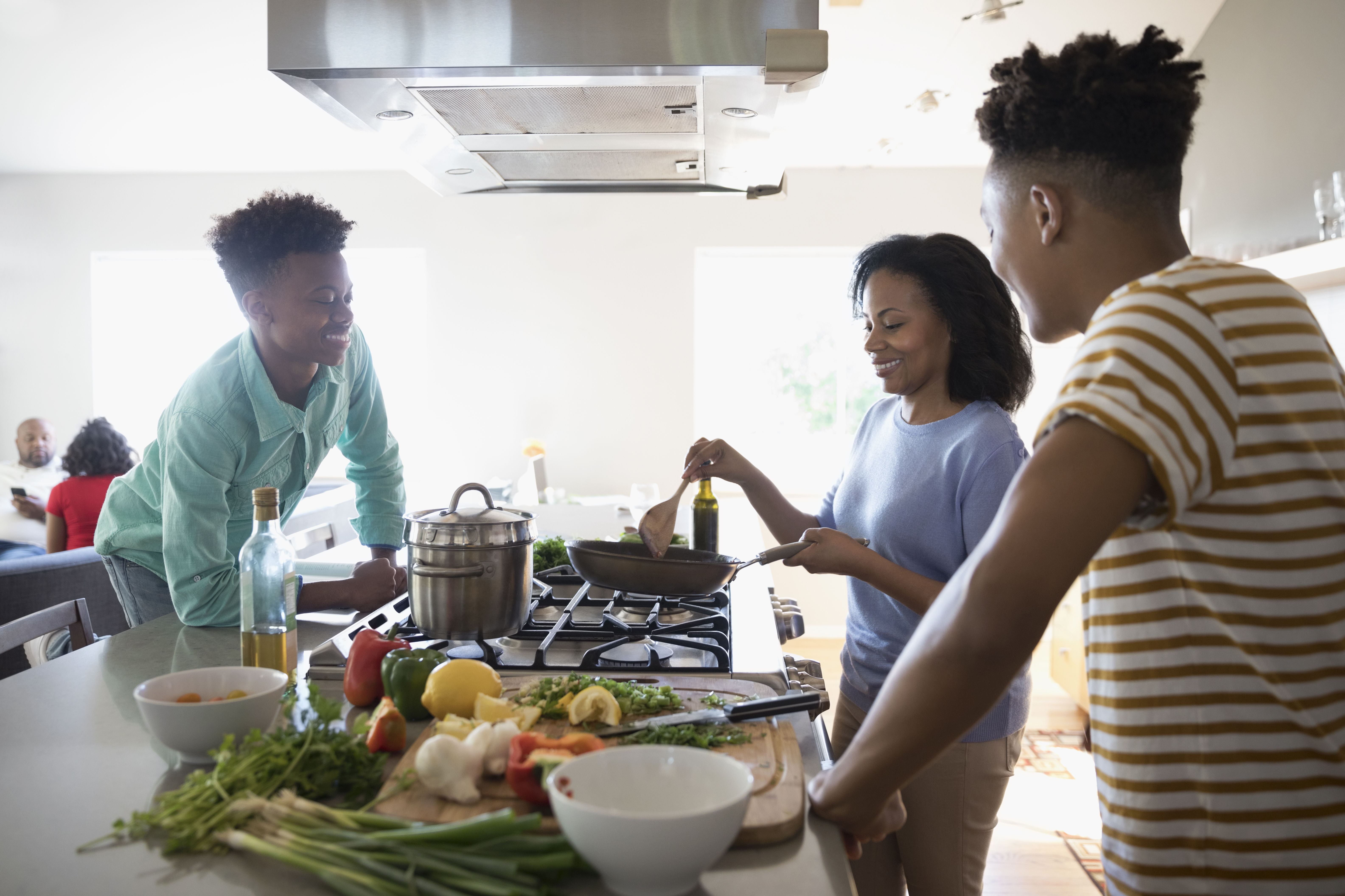 African American mother and teenage sons cooking at stove in kitchen