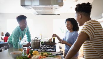 African American mother and teenage sons cooking at stove in kitchen