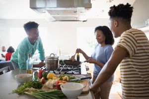 African American mother and teenage sons cooking at stove in kitchen