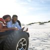 Couple with digital tablet in jeep on beach