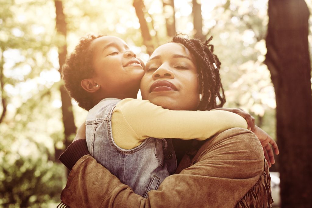 African American mother and her daughter hugging with daughter in forest.