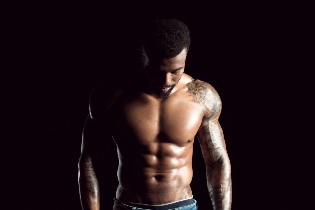 Tattooed physical athlete in front of black background