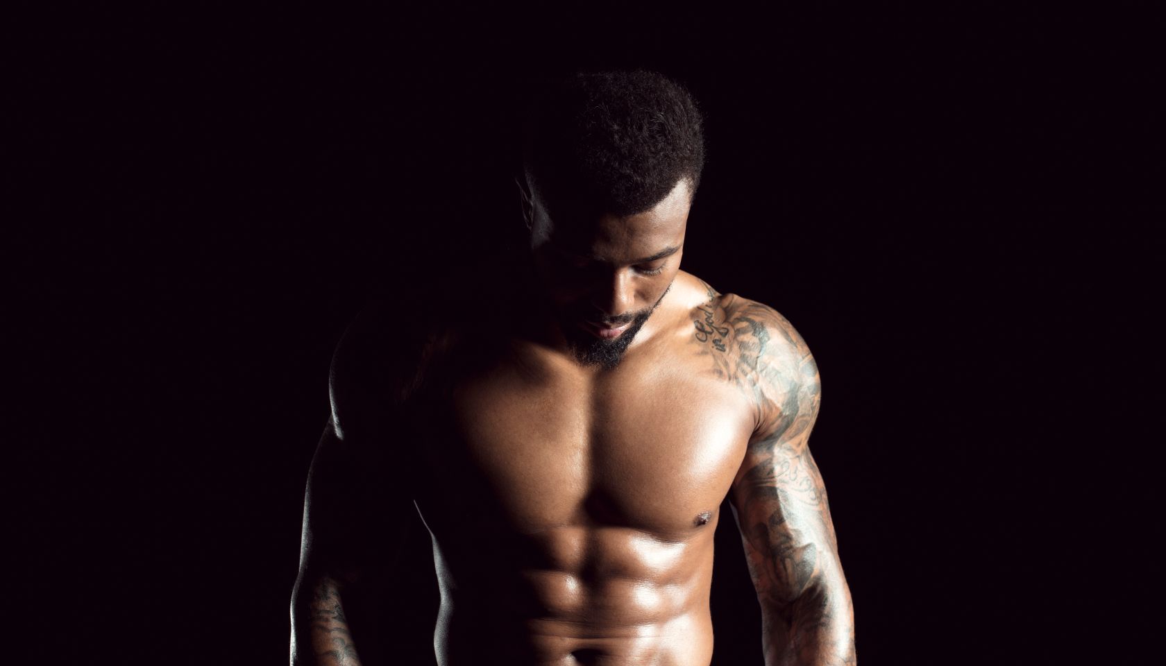 Tattooed physical athlete in front of black background