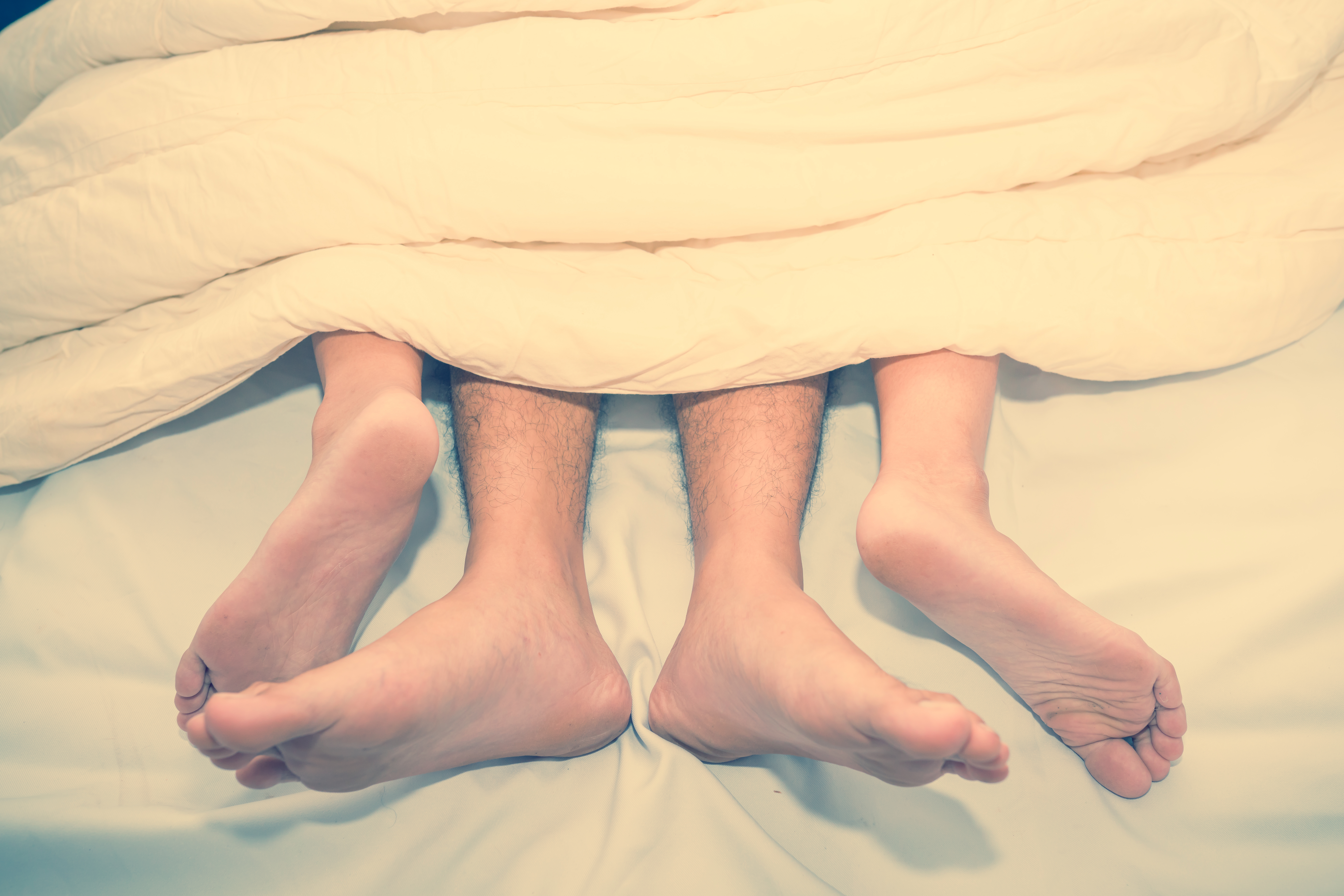 Low Section Of Couple Relaxing On Bed At Home