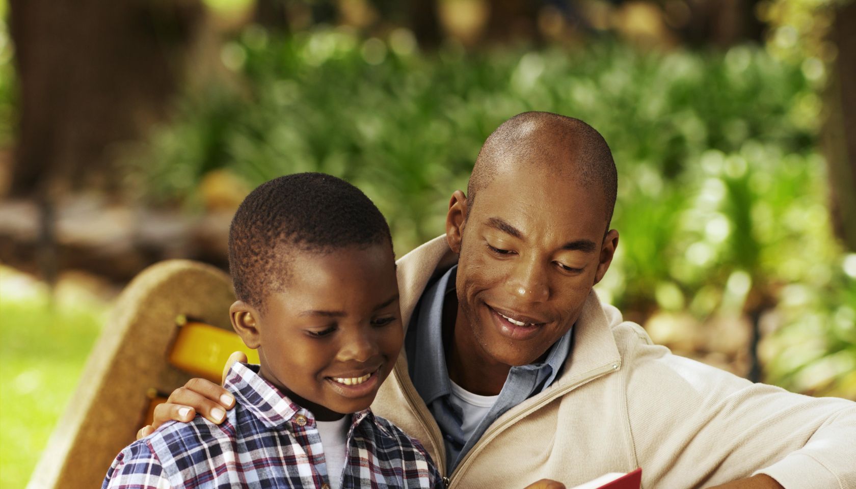 Close-up of father and son sitting on bench reading book (10-11)