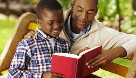 Close-up of father and son sitting on bench reading book (10-11)