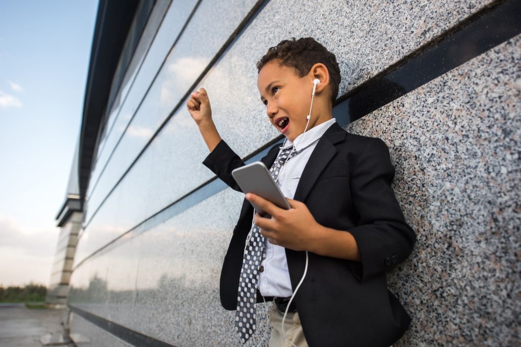 Small African American business boy singing while listening MP3 player.