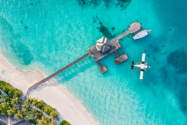 Beautiful aerial view of Maldives shore, pier villa seaplane top view, wooden boat Dhoni and tropical beach. Palm trees white sand, sea. Luxury travel and vacation concept. Amazing aerial landscape