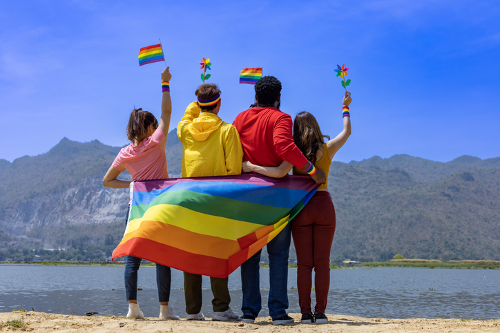 Back view of transgender and gender fluid group and homosexual people celebrating LGBTQ+ pride month in colorful dress and rainbow flag to embrace the difference and understanding concept