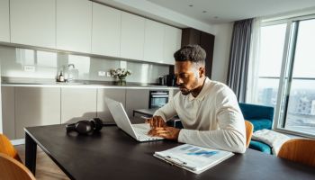 African American mid adult financial advisor working from home on laptop and investing into crypto currencies