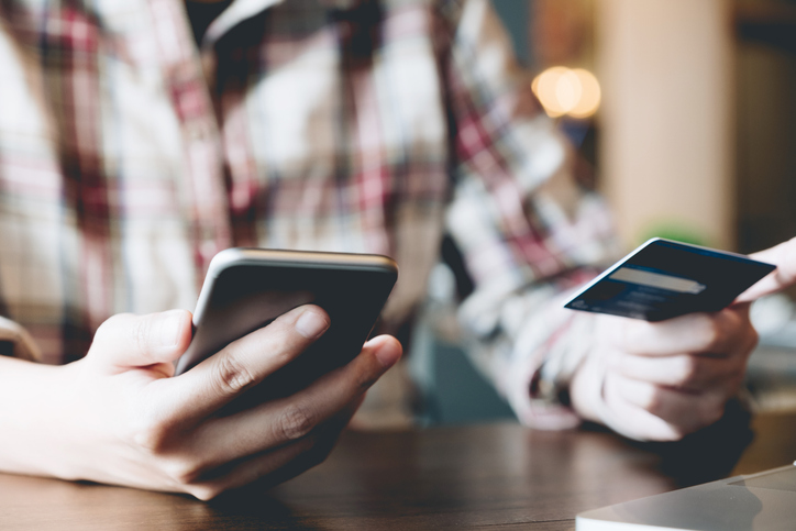 Midsection Of Man Using Smart Phone While Making Online Payment At Table
