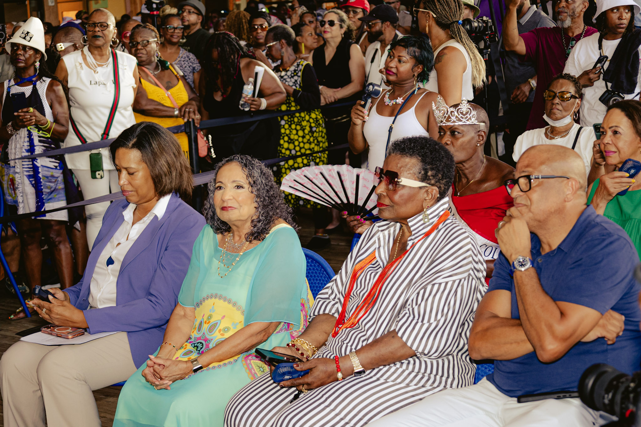 Diverse crowd of people gathered at a nighttime event, some wearing colorful, festive attire and accessories.