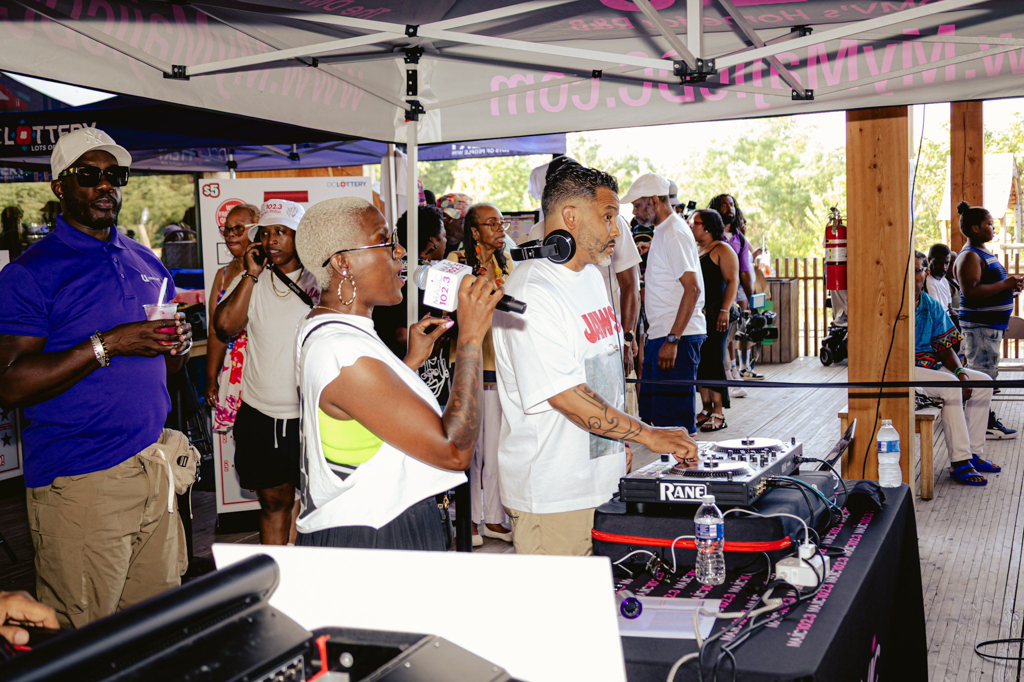 Outdoor event with a crowd of people, some holding microphones, in front of a tent with branding for "Lotto" and "Rane".